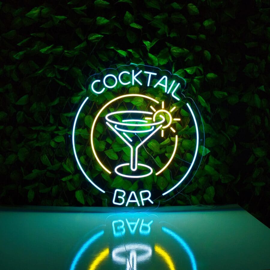 Cartel de Neón Cocktail Bar con una copa de cóctel y las palabras "cocktail bar" sobre un fondo de hojas verdes.