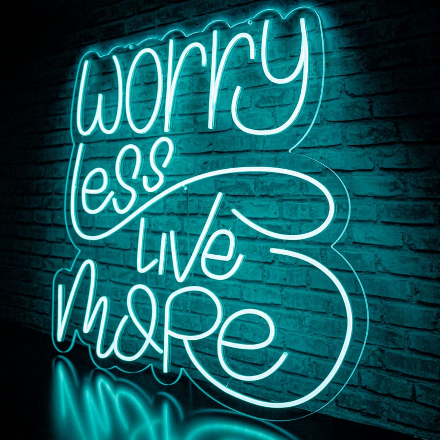 Neón Worry Less Live More en una pared de ladrillos con la frase "Preocúpate menos, vive más" en letra cursiva e iluminado con luces azul verdosas.