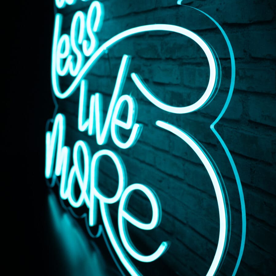 Un letrero de neón en letras cursivas azules en una pared de ladrillos dice "Neón Worry Less Live More".