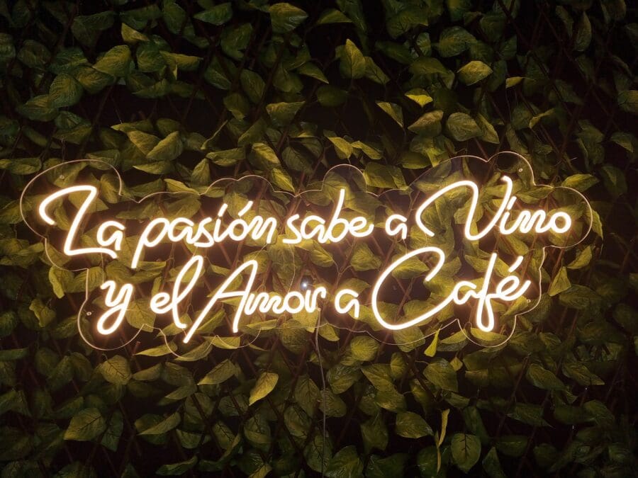 Neón La pasión sabe a vino y el amor un café iluminado sobre un fondo de hojas verdes.