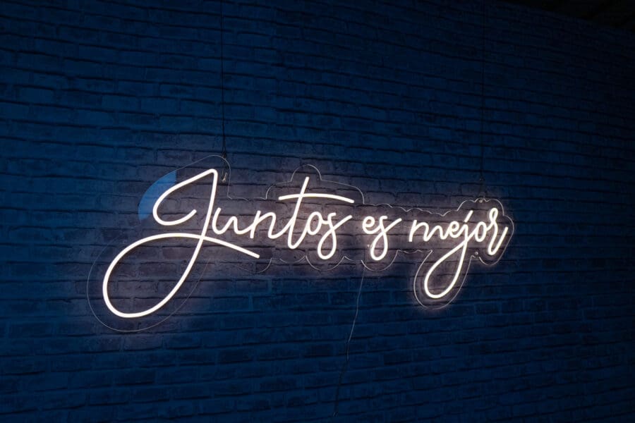 El Neón blanco Juntos es Mejor en una pared de ladrillo azul dice "Juntos es mejor" traducido del español como "Juntos es mejor".