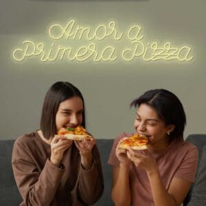Dos mujeres disfrutando de Neón "Amor a primera pizza" frente a un cautivador letrero de neón.
