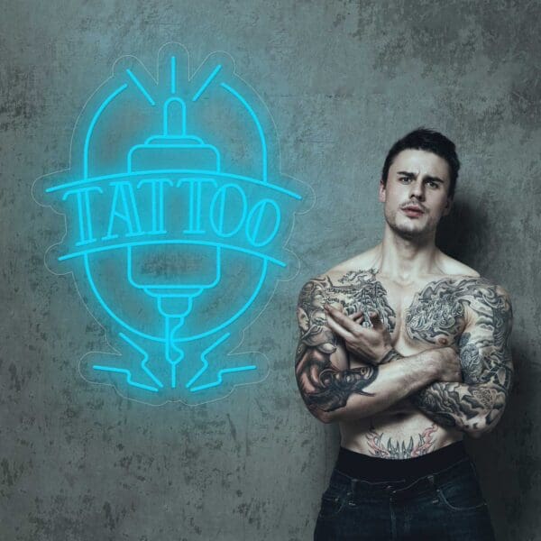 Un hombre con tatuajes posa frente a Neón Tattoo Aguja.