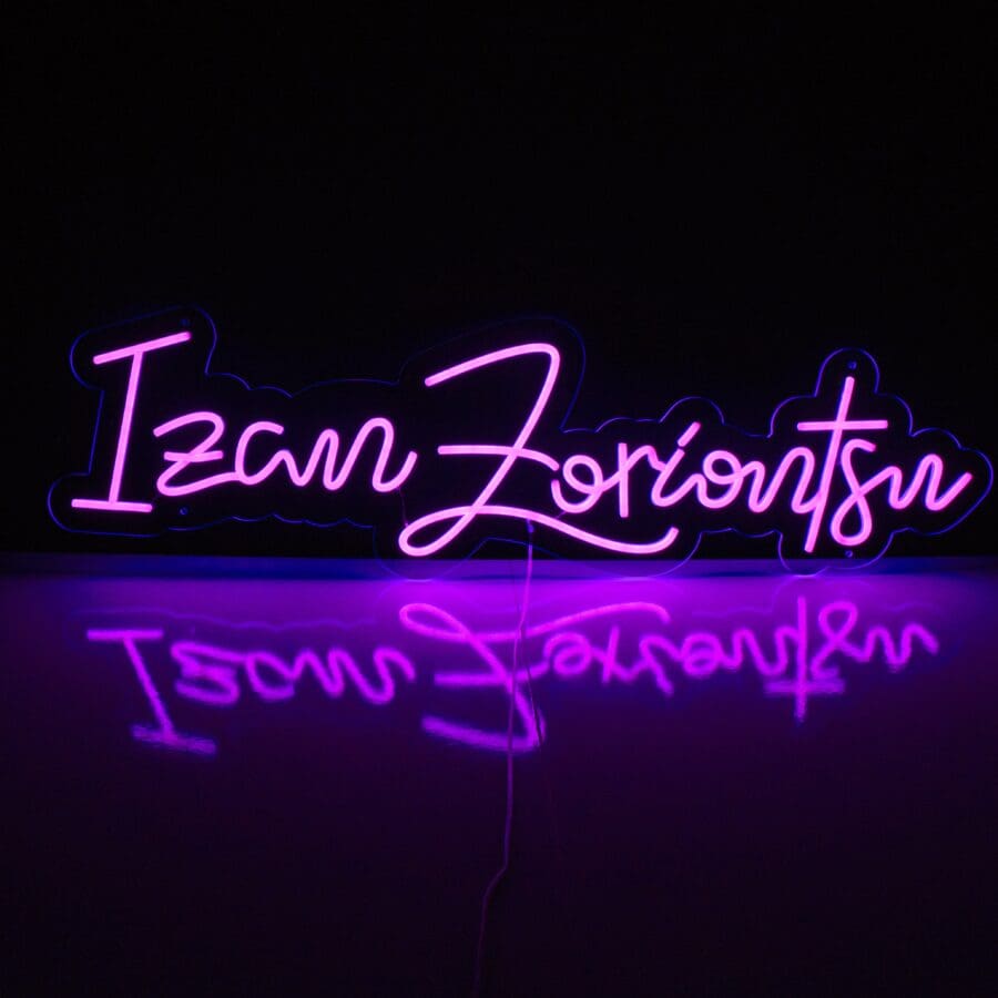 A Letras en Neón Personalizadas muestra el texto "Izan Zoriontsu" en cursiva con iluminación violeta, sobre un fondo oscuro y reflejándose en una superficie brillante.