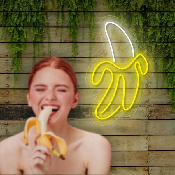 Una mujer está comiendo un Neón Banana frente a un letrero de neón en un estudio de tatuajes.
