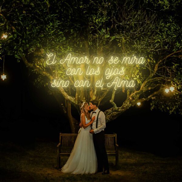 Un hombre y una mujer compartiendo un beso apasionado, Neón El Amor no se mira con los ojos sino con el Alma, iluminado bajo un árbol.
