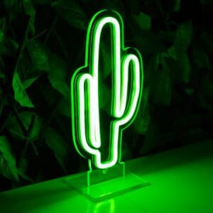 Una Lámpara de Néon Cactus verde sobre una mesa frente a una planta.