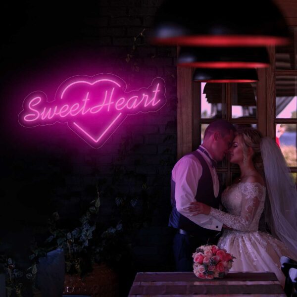 Una novia y un novio besándose frente a un letrero de neón que dice Neón Sweet Heart.
