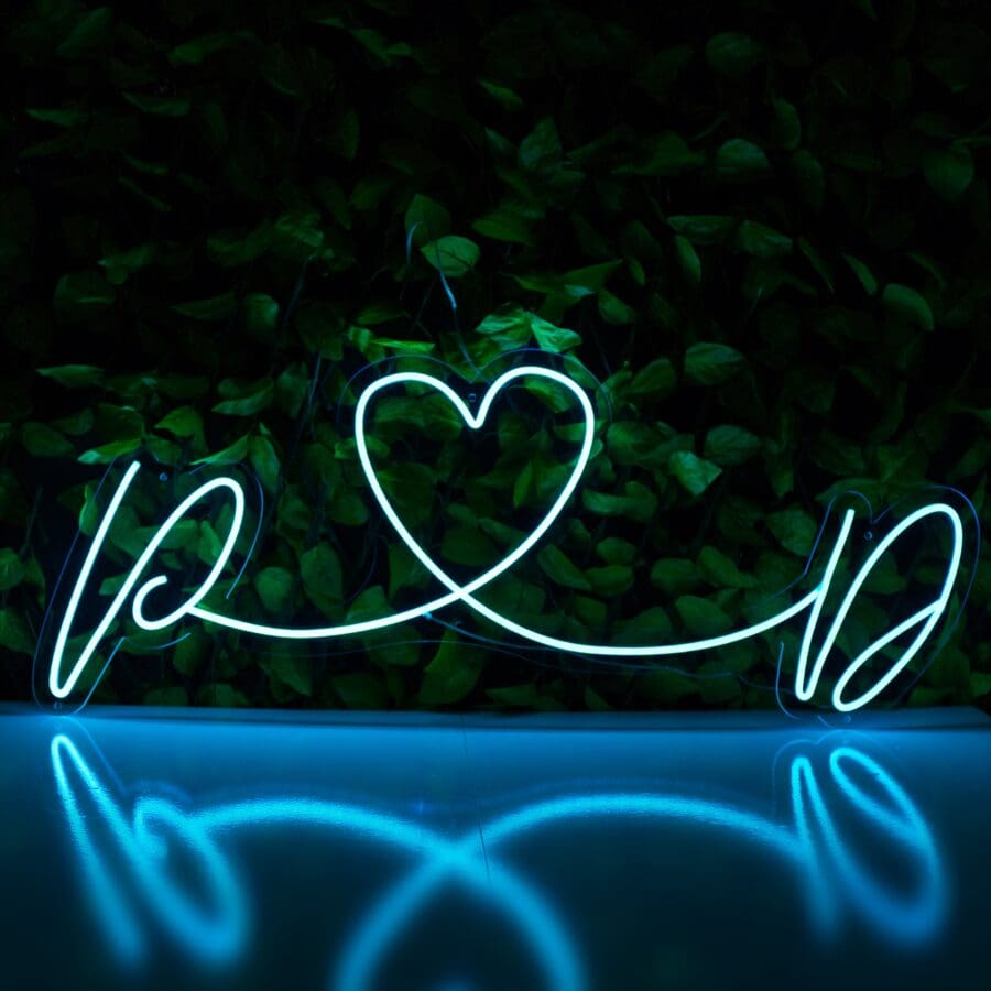 Una Boda Neón Personalizado en forma de corazón con estelas de luz sobre un fondo de follaje verde oscuro.