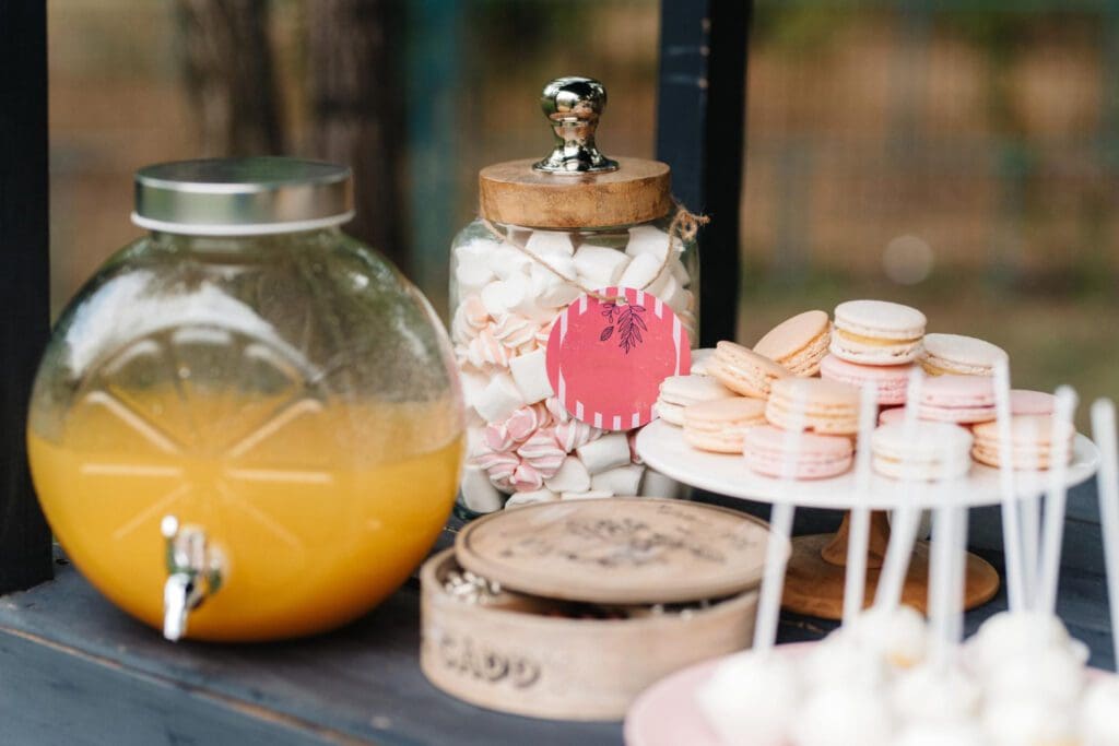 Una mesa de postres con zumo de naranja, galletas y macarons.