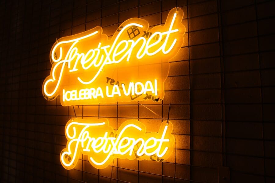 Letrero de neón en una pared de ladrillos que muestra la palabra "freixenet" y la frase "te ayuda a celebrar la vida".