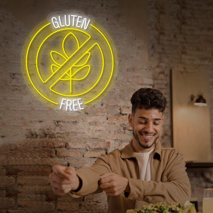Hombre sonriendo mientras come una ensalada en una mesa, con un letrero Neón Gluten Free iluminado en la pared de ladrillo detrás de él.