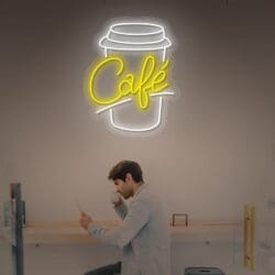 Un hombre en una cafetería, leyendo un menú, con un brillante letrero de neón con forma de taza de café