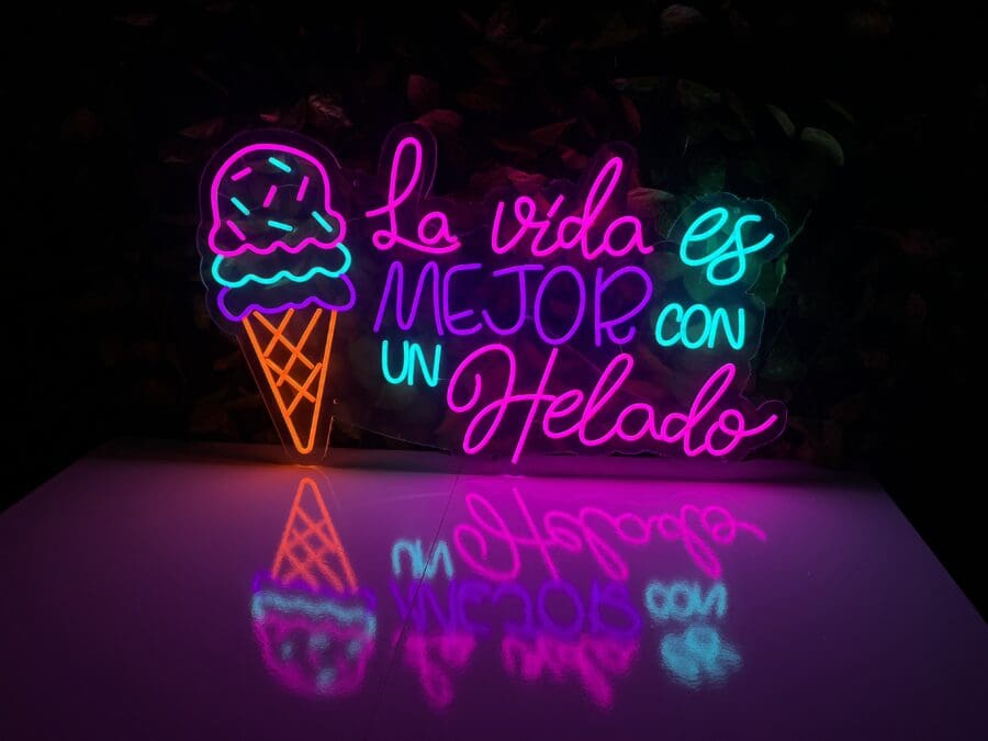 Neón La Vida es Mejor con un Helado con un cono de helado y el texto en español "La vida es mejor con un helado" reflejado en una superficie brillante.