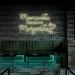 Un bar con asientos de terciopelo verde, una pared de ladrillos y un Neón Mamasita Needs a Margarita con una imagen de una copa de martini, perfecto para cuando quieras tomarte una selfie.