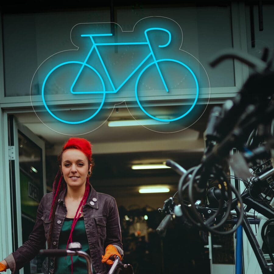 Una persona pelirroja se encuentra frente a una tienda de bicicletas bajo un letrero de neón, con varias bicicletas visibles en primer plano.