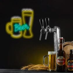 Un grifo de cerveza y varias botellas de cerveza se muestran sobre una superficie de madera con un letrero de neón que muestra una jarra de cerveza y un vaso de cerveza y la palabra "Cerveza" en el fondo.