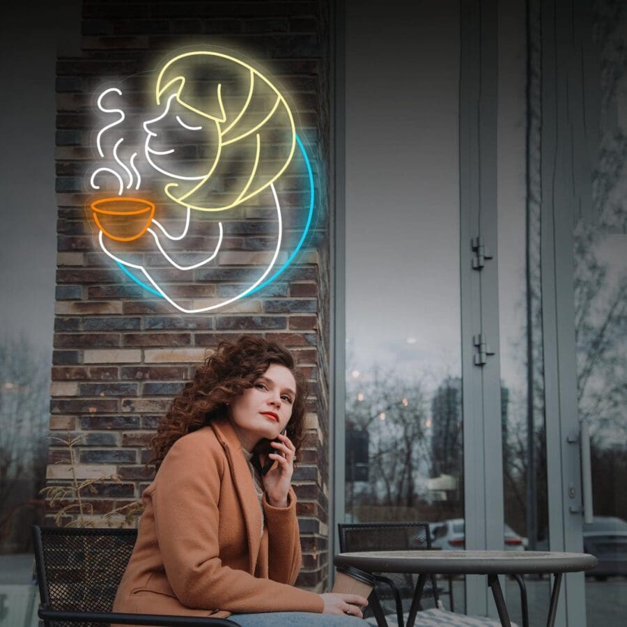 Una mujer de pelo rizado está sentada en una mesa de café al aire libre, hablando por teléfono. Detrás de ella, en la pared de ladrillos, hay un cartel de neón de una mujer bebiendo una bebida caliente.