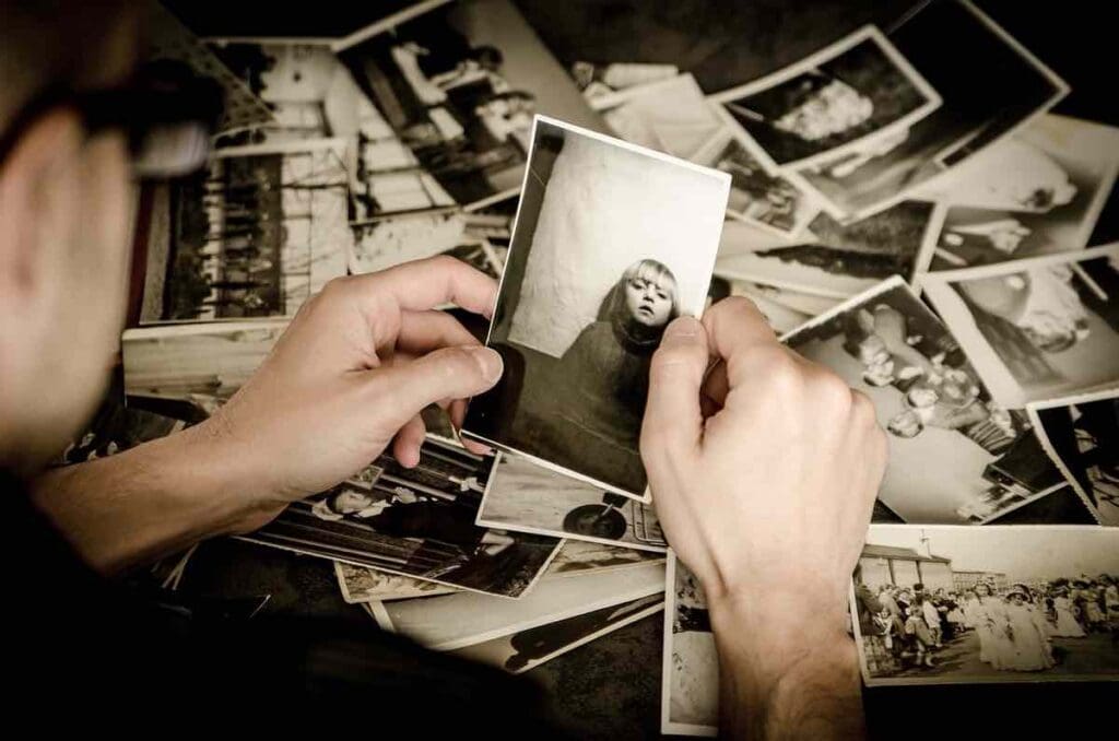 Una persona sostiene una fotografía en blanco y negro de un niño, rodeada de una colección dispersa de fotografías antiguas sobre una mesa.