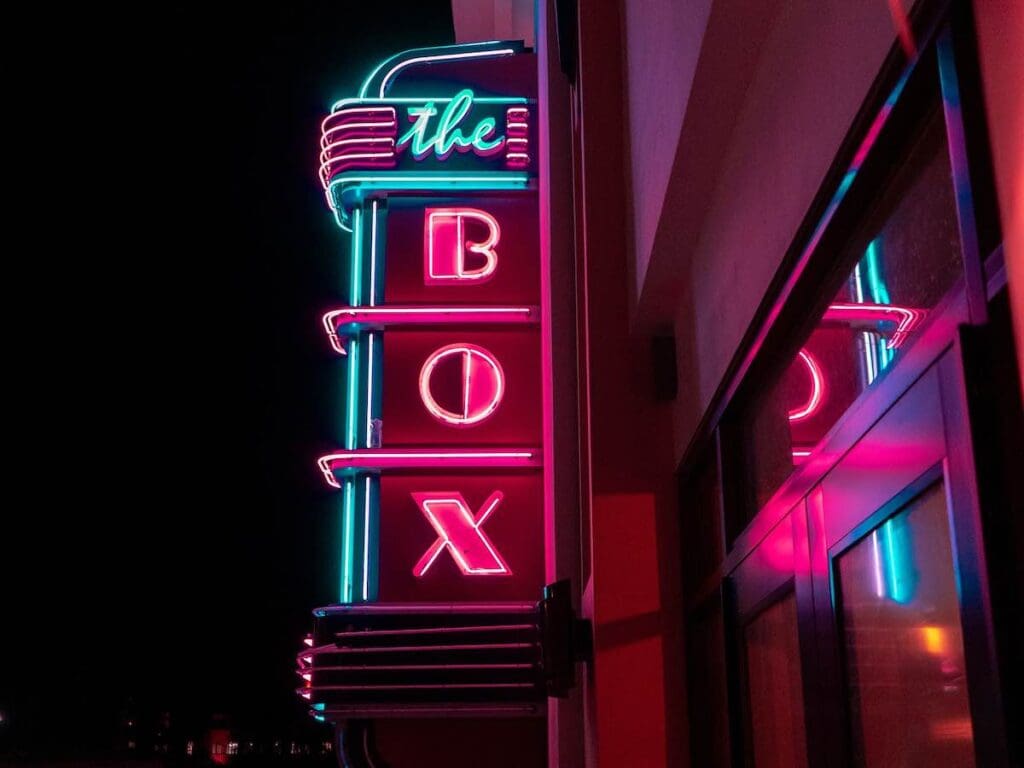 Letrero de neón que dice "The Box" con luces rojas y azules, montado en un edificio por la noche.