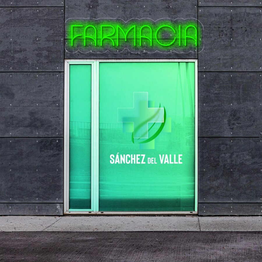 Letrero de neón que dice "Farmacia" sobre una puerta de vidrio verde con una cruz médica y "Sánchez del Valle" impreso en ella. La puerta está empotrada en una pared de hormigón gris.