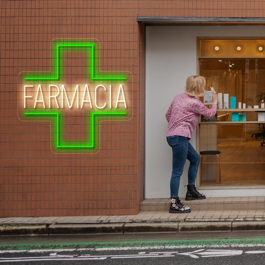 Persona mirando hacia una farmacia con un cartel en forma de cruz verde neón que dice "FARMACIA" en la pared.