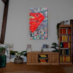 En la sala de estar hay una pared decorada con un llamativo motivo de cómic y un logotipo de Superman en neón. Debajo, un armario de madera muestra libros y plantas. A la derecha, hay una estantería con libros de colores.