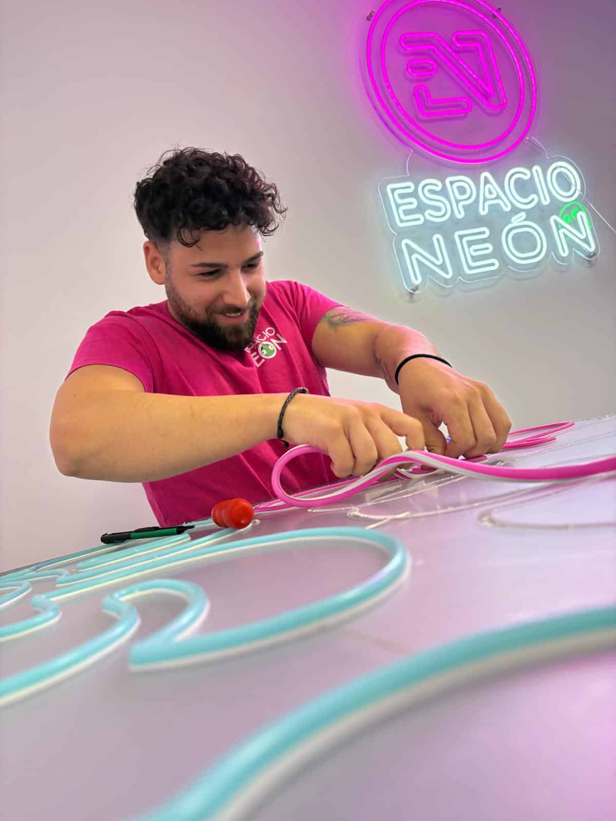 Artesano de Espacio Neón dando forma a tubos de neón LED sobre la mesa de trabajo del taller.