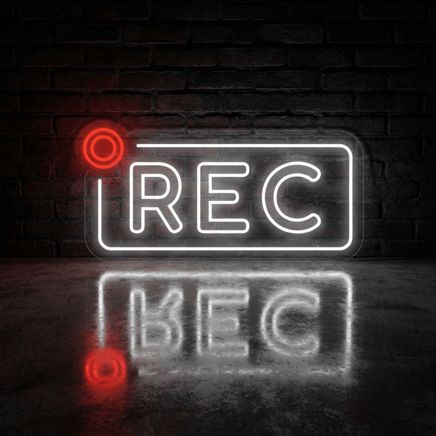 Cartel de neón que muestra "REC" con un punto rojo, iluminado contra una pared de ladrillo oscuro, reflejándose en una superficie brillante.