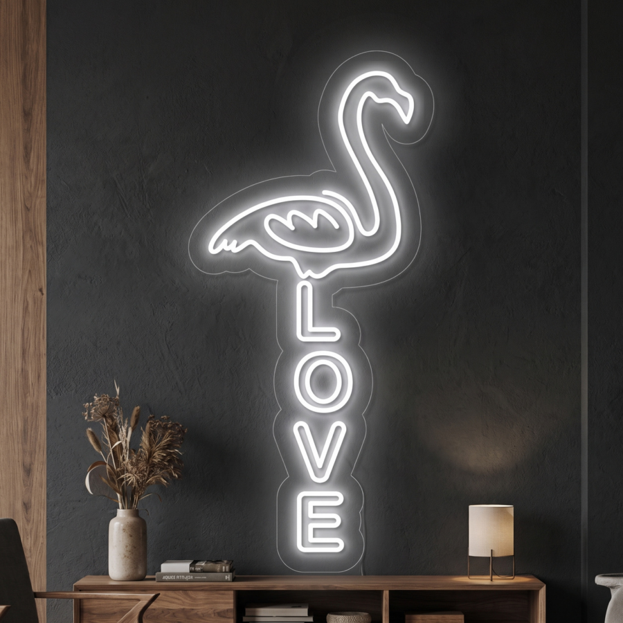 Letrero de neón con forma de flamenco y la palabra «LOVE» escrita en vertical debajo, que brilla en blanco sobre una pared oscura, situado encima de una estantería con objetos decorativos y una lámpara.