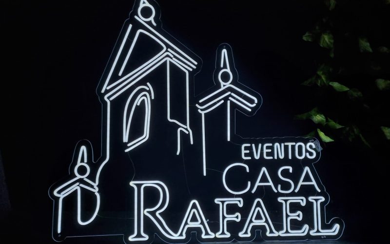 Letrero de neón que representa un edificio con el texto "EVENTOS CASA RAFAEL" iluminado sobre un fondo oscuro.