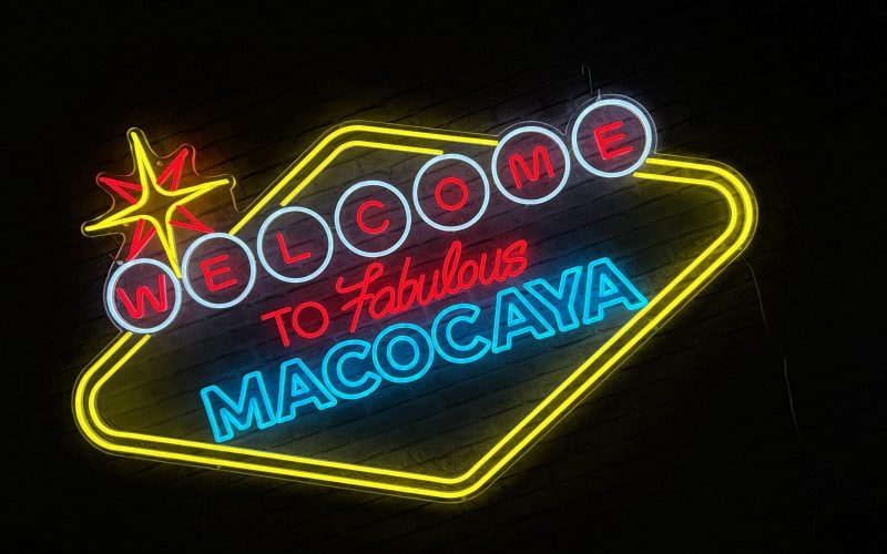 Letrero de neón que dice "Bienvenido a Fabulous Macocaya" con un símbolo de estrella roja en la parte superior izquierda.