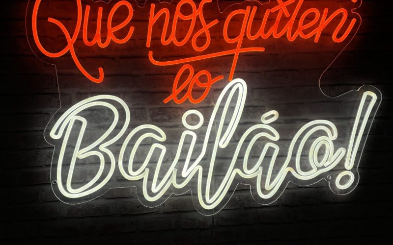 El letrero de neón con texto rojo y blanco sobre un fondo oscuro dice "¡Que nos quiten lo bailao!" en español.